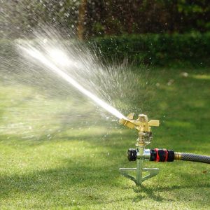 The Eden Impulse Sprinkler Head shown connected to a step spike base and spraying water over a green lawn