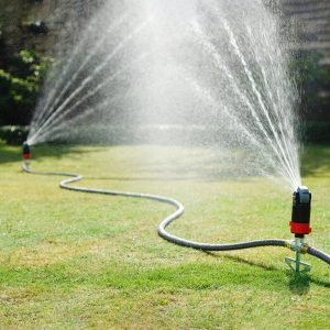 Two Eden Multi-Pattern Sprinkler Plus Misting System with Step Spikes shown connected in a series watering a large, green lawn