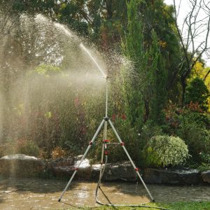 Eden PRO Metal Telescoping Tripod with Brass Impulse Sprinkler spraying water towards a garden